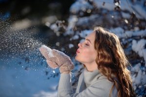 Femme qui souffle sur de la neige, en fond un paysage de neige.