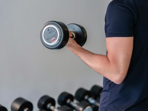 homme qui fait du renforcement des biceps avec un poids, vue moitié profil, on ne voit pas sa tête